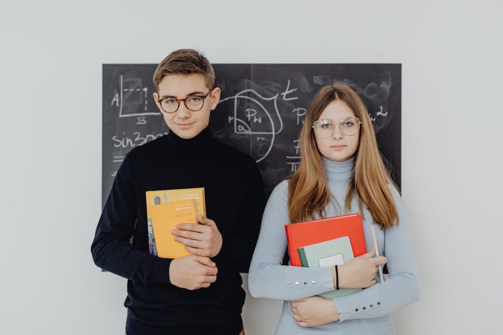 Photo of a male and female student holding books in front of a blackboard